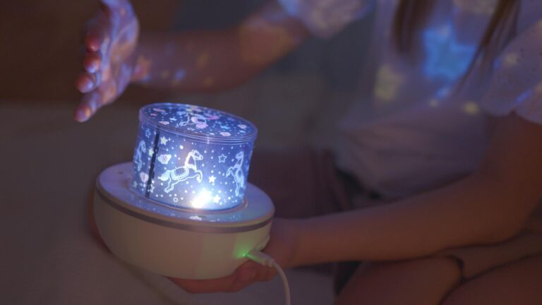 A child's hand near an illuminated decorative lamp projecting patterns in a dark room.